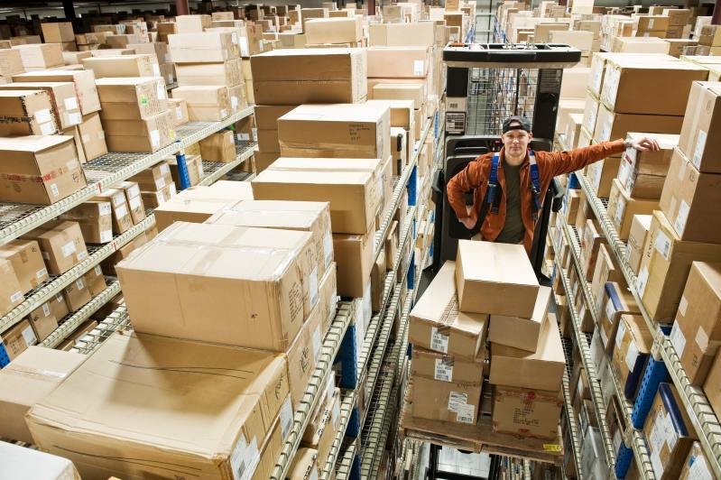 A warehouse worker standing on a motorized stock picker with boxes in a distribution warehouse.